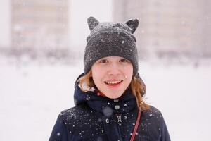 Portrait of happy 12-year-old girl in a warm jacket and a cat-ear hat under heavy snow photo