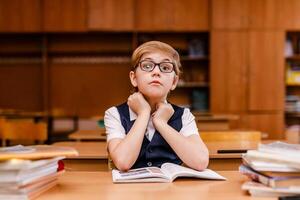 8-year-old schoolboy in glasses, white shirt, and vest studying and reading books in classroom photo
