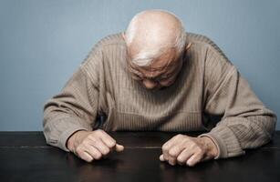 Senior man feeling headache and negative emotions while sitting at the table photo