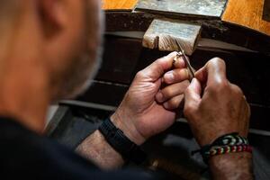 Goldsmith working and creating in his crafting gold jewelry workshop. Jeweler liming a silver jewel. photo