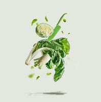 Flying green vegetables selection with knife at light background. Ingredients for healthy eating lettuce, fennel, bok choy and edamame levitating in the air. Front view. photo