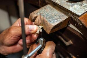 Goldsmith working and creating in his crafting gold jewelry workshop. Jeweler sawing a silver jewel. photo