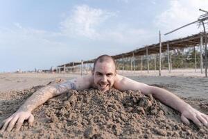 Happy young caucasian man enjoying the beach, laying on the sand and smiling at the camera photo