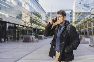 A handsome businessman is talking on the cell phone near his office photo