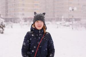 Portrait of 12-year-old girl in a warm jacket and a cat-ear hat under heavy snow photo