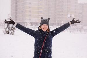 Portrait of an happy 12-year-old girl in a warm jacket and a cat-ear hat under heavy snow photo