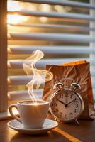 Steaming coffee cup and alarm clock by sunrise at window photo