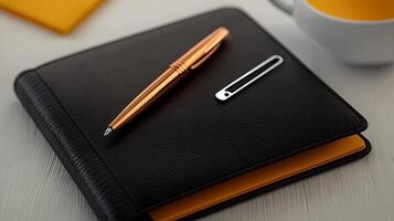 A sleek black notebook with a golden pen and paperclip on a white table, with a yellow background photo