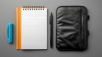 Stationery setup featuring a notepad, pen, highlighter, and a black case on a gray surface photo