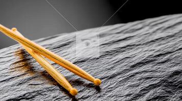 Close-up of yellow chopsticks resting on a textured black stone surface, showcasing minimalist elegance photo