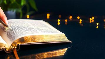 Open book with a hand turning the page, surrounded by soft glowing lights and greenery photo