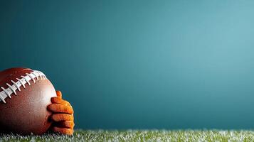 A close-up of a football cradled in an orange-gloved hand on a grassy field with a blue background photo