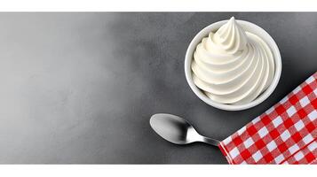 Creamy soft-serve ice cream in a bowl on a gray surface with a checkered napkin and spoon photo