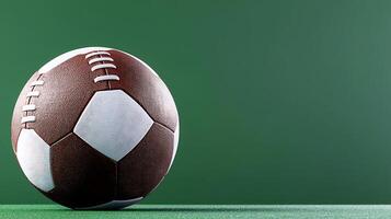 A close-up of a brown and white soccer ball resting on green turf against a solid background photo