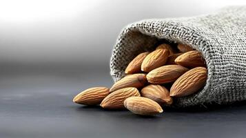 A burlap sack spilling fresh almonds on a dark surface with a soft gradient background photo