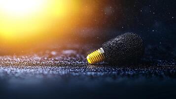 Close-up of a textured black microphone on a reflective surface with a warm light backdrop photo
