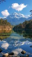 Snowy mountain reflecting in a pristine lake with pine trees and clouds photo