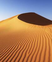 Sand dune formation under clear blue sky in desert photo