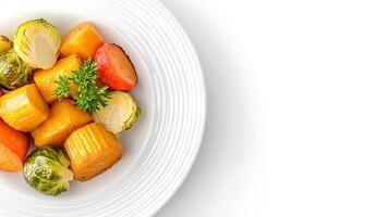 Colorful assortment of roasted vegetables on a white plate, garnished with fresh herbs photo
