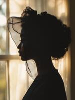 Silhouette of a person wearing a silk bonnet by a sunlit window photo