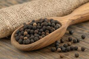 Black peppercorns resting in wooden spoon on rustic table photo