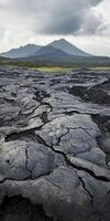 Cracked lava landscape with distant volcano under cloudy sky photo