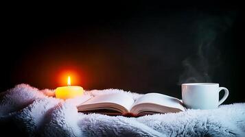 Cozy scene with an open book, steaming cup, and candle on a soft blanket in dim light photo