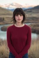 A woman in a red sweater stands in front of a river photo