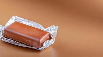 A close-up of a chocolate bar partially wrapped in foil on a smooth brown background photo