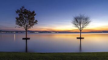 Serene sunset over a calm lake with two distinct trees reflecting in the water photo