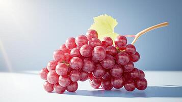 A cluster of fresh red grapes with a green leaf, illuminated by soft sunlight, on a light blue background photo
