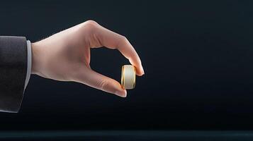 A close-up of a hand holding a shiny gold ring against a dark background, symbolizing elegance photo