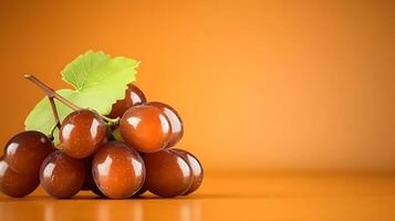 A cluster of glossy brown grapes resting on an orange background with a green leaf accent photo