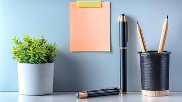 A neatly arranged workspace featuring stationery, a plant, and a blank sticky note for reminders photo