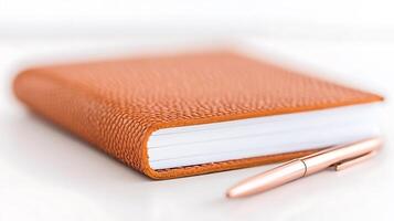 Close-up of an elegant orange leather notebook with a sleek pen resting beside it on a white surface photo