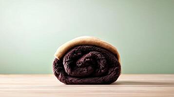 Soft, rolled-up blanket resting on a wooden surface against a muted green background photo