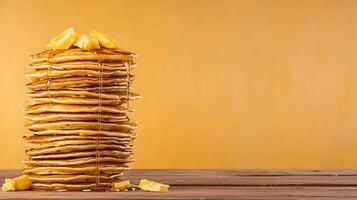 Stacked pancakes drizzled with syrup on a wooden table against a warm yellow background photo