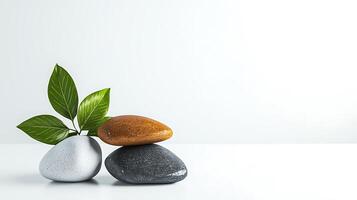 Three smooth stones stacked with green leaves on a minimalist white background, symbolizing balance photo