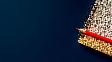 Vibrant red pencil resting on textured notebook against a deep blue background, ideal for creative projects photo