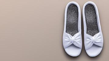 White slippers with a bow design resting on a smooth beige surface, ideal for fashion displays photo