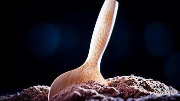 Wooden scoop resting in a mound of cocoa powder with a dark, blurred background photo