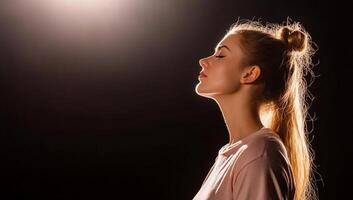 A serene profile of a woman illuminated against a dark background. photo