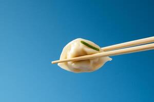 A dumpling held with chopsticks against a blue background. photo