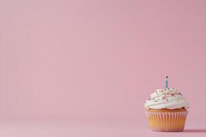 A decorated cupcake with a candle against a pink background. photo
