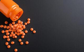 Orange pills spilling out of a bottle on a black background photo