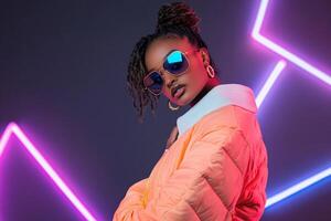A woman wearing sunglasses and an orange jacket in front of neon lights photo