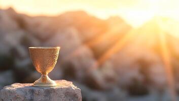 A golden chalice sits on a rock, illuminated by a sunset glow. photo