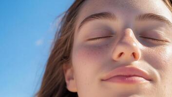 A close-up of a serene young woman with closed eyes against a blue sky. photo