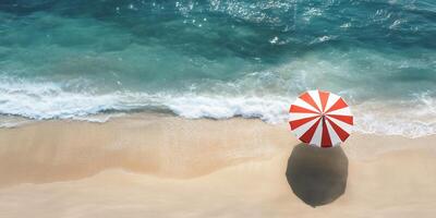 Aerial view of a beach with a red and white umbrella by the shore. photo
