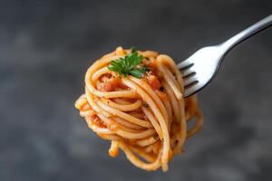 A fork holding a serving of spaghetti with sauce and garnish. photo